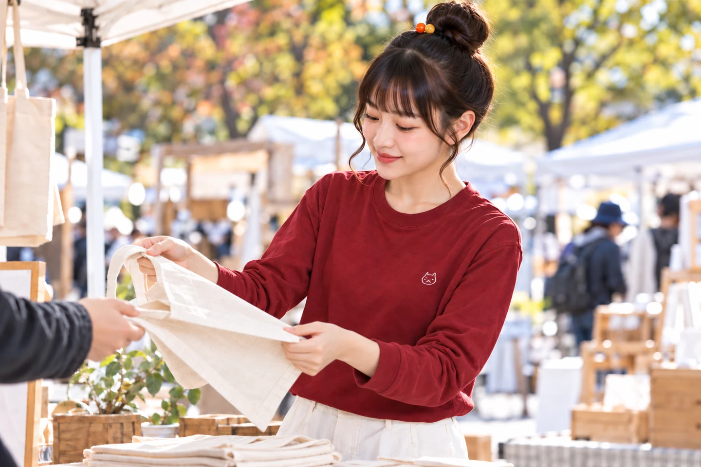 地域イベントの会場でバーガンディの長袖Tシャツを着て、手渡しの準備をする看板娘